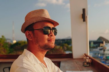 Handsome young Asian man wearing sunglasses smiling and enjoying the sunset scenery at Labuan Bajo beach.