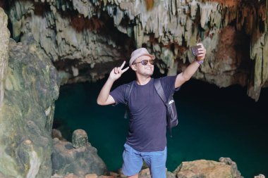 Joyful young Asian man using his smartphone to take picture while enjoying holiday at Rangko Cave, Labuan Bajo, Indonesia.