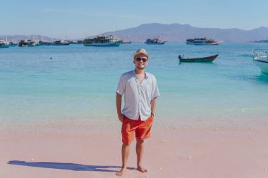 Handsome young Asian man wearing shirt and beach hat smiling at the camera in Pink Beach, Labuan Bajo.