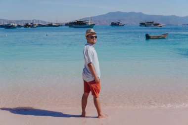 Handsome young Asian man standing and smiling over his shoulder to the camera at Pink Beach, Labuan Bajo.