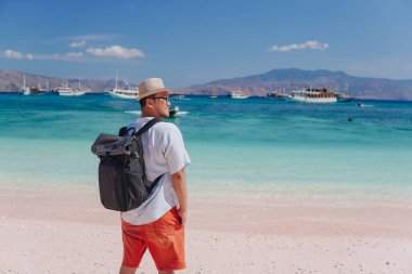 Back view of young Asian man with a backpack is enjoying scenery at Pink Beach, Labuan Bajo.