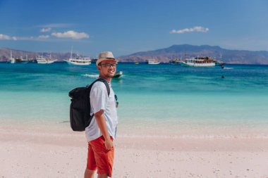 Back view of young Asian man with a backpack is enjoying scenery at Pink Beach, Labuan Bajo.