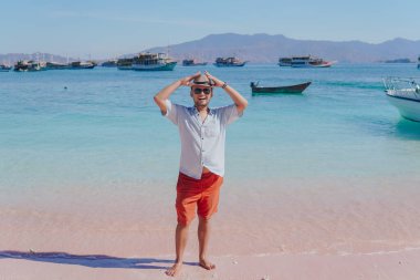 Handsome young Asian man wearing shirt and beach hat smiling and enjoying holiday at Pink Beach, Labuan Bajo.