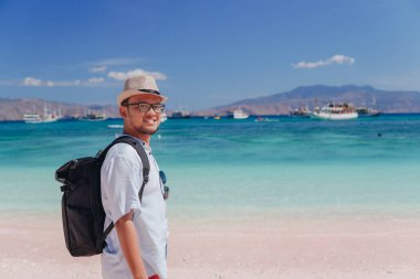 Back view of young Asian man with a backpack is enjoying scenery at Pink Beach, Labuan Bajo.