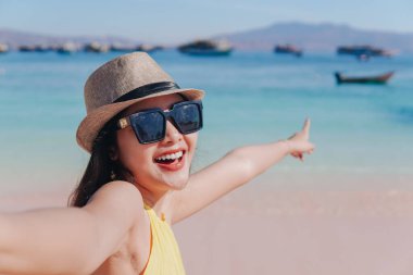 Cheerful young Asian woman holding hands with a man on Pink Beach, Labuan Bajo while pointing to the scenery.