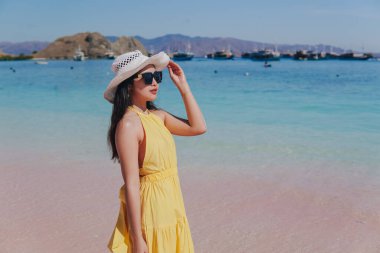 Back view of a carefree young Asian woman wearing yellow dress standing and enjoying the pink beach scenery in Labuan Bajo.