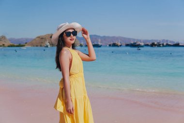 Back view of a carefree young Asian woman wearing yellow dress standing and enjoying the pink beach scenery in Labuan Bajo.