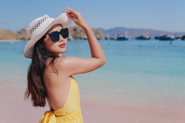 Back view of a carefree young Asian woman wearing yellow dress standing and enjoying the pink beach scenery in Labuan Bajo.