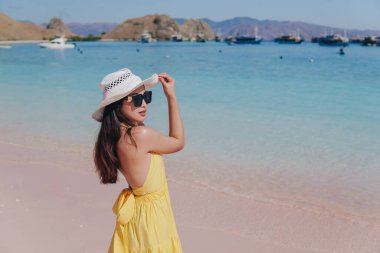 Back view of a carefree young Asian woman wearing yellow dress standing and enjoying the pink beach scenery in Labuan Bajo.
