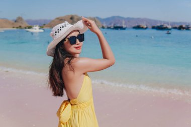 Back view of a carefree young Asian woman wearing yellow dress standing and enjoying the pink beach scenery in Labuan Bajo.