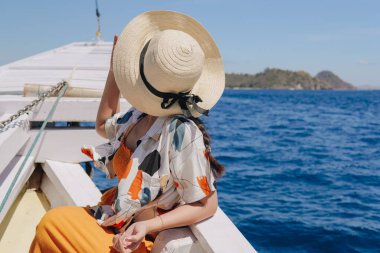 Hasır şapkalı genç bir Asyalı kadının arkadan görünüşü Labuan Bajo sahnesinin tadını çıkarıyor..