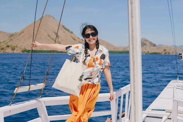 Teknede durup Labuan Bajo deniz manzarasının keyfini çıkarırken kameraya gülümseyen mutlu genç Asyalı kadın..