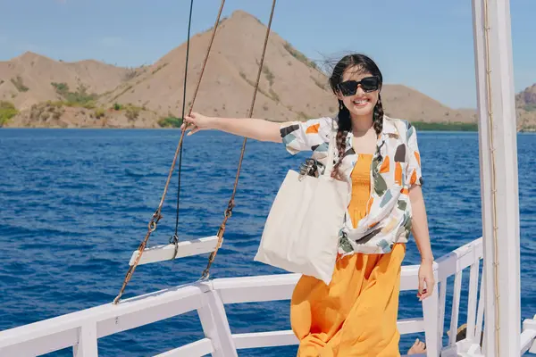 Teknede durup Labuan Bajo deniz manzarasının keyfini çıkarırken kameraya gülümseyen mutlu genç Asyalı kadın..