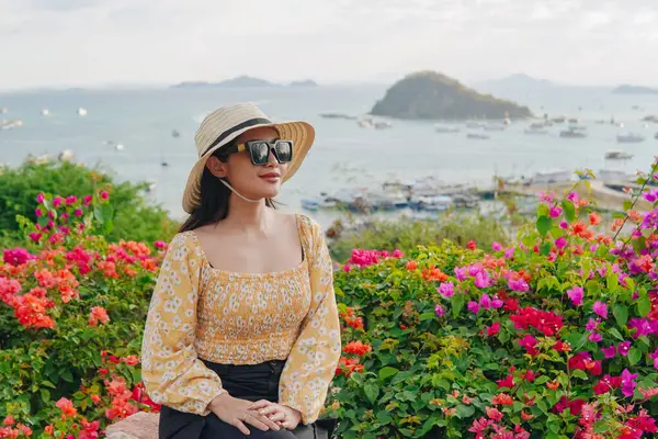 Hasır şapka ve güneş gözlüğü takan genç Asyalı kadın Puncak Waringin, Labuan Bajo 'da manzaranın tadını çıkarıyor..