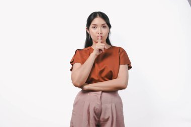 Ciddi bir Asyalı kadın kahverengi gömlek giyer ya da beyaz arka planla izole edilmiş parmaklarıyla susar..