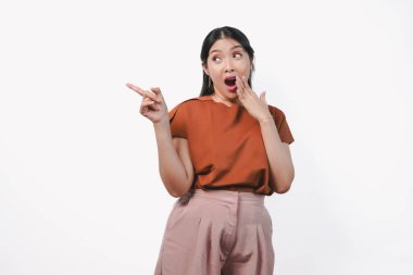 Kahverengi tişörtlü güzel bir Asyalı kadın beyaz arka planla izole edilmiş, şok olmuş bir ifadeyle fotokopi odasını işaret ediyor..