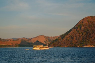 Large white boat sailing in the ocean at golden hour in Labuan Bajo sea with mountain in the background.