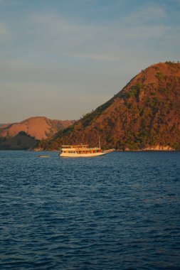 Large white boat sailing in the ocean at golden hour in Labuan Bajo sea with mountain in the background.