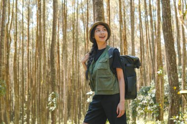 Happy young Asian woman walking through the forest bringing a backpack, enjoying her time in nature.
