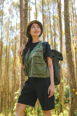 Happy young Asian woman walking through the forest bringing a backpack, enjoying her time in nature.