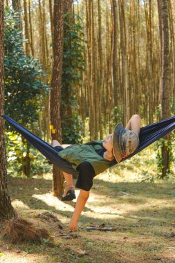Yeşil yelek giyen yorgun genç Asyalı kadın hamakta uzanıyor, ormanda uyuyor..