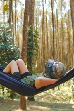 Yeşil yelek giyen yorgun genç Asyalı kadın hamakta uzanıyor, ormanda uyuyor..