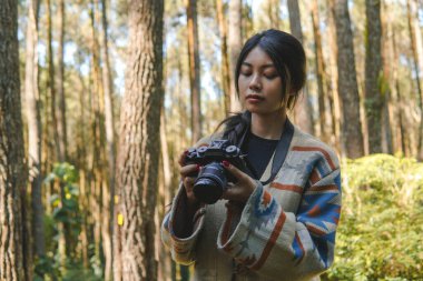 Güzel genç Asyalı kadın orman manzarasının tadını çıkarırken elinde bir kamera tutuyor..