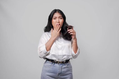 Beyaz gömlekli ve kotlu üzgün genç Asyalı kadın beyaz arka planla izole edilmiş kuru ve hasarlı saçlarını tutuyor..