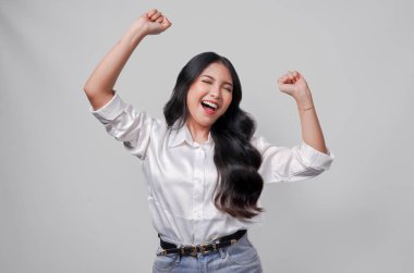 Beyaz gömlekli heyecanlı genç Asyalı kadın mutlu ve başarılı bir ifadeyle, beyaz arka planla izole edilmiş..