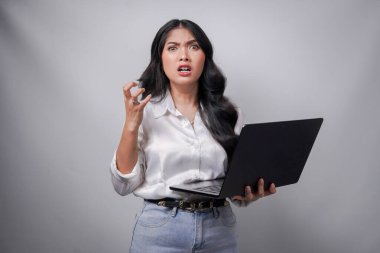 Beyaz tişörtlü kafası karışmış genç Asyalı kadın dizüstü bilgisayarını tutuyor. Baş ağrısı çekiyor, beyaz arka planda izole edilmiş..