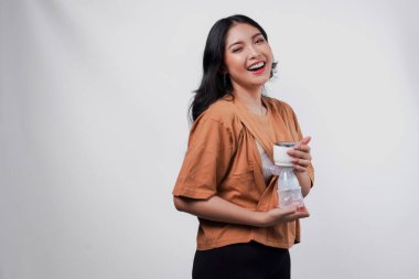 Mutlu genç Asyalı anne süt pompalıyor otomatik göğüs pompası makinesiyle, beyaz arka planla izole edilmiş.