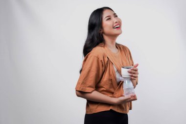 Mutlu genç Asyalı anne süt pompalıyor otomatik göğüs pompası makinesiyle, beyaz arka planla izole edilmiş.