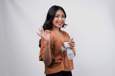 Gülümseyen Asyalı anne beyaz arka planla izole edilmiş parmak hareketi yaparken otomatik göğüs pompası ile anne sütü pompalıyor..