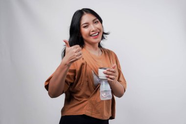 Güzel Asyalı anne, beyaz arka planla izole edilmiş baş parmak hareketi yaparken otomatik göğüs pompası ile anne sütü pompalıyor..