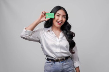 Beyaz gömlek giyen neşeli genç Asyalı kadın, beyaz arka planla izole edilmiş bir kredi kartı sunuyor..