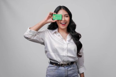 Beyaz gömlek giyen neşeli genç Asyalı kadın, beyaz arka planla izole edilmiş bir kredi kartı sunuyor..