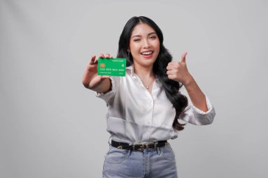 Neşeli genç Asyalı kadın kredi kartı ya da banka kartı sunarken parmak hareketi yapıyor, beyaz arkaplanla izole edilmiş..