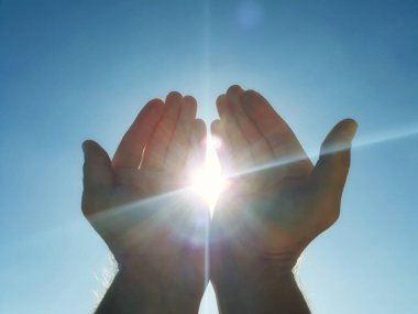 Mavi gökyüzü ile güneşi tutan erkek eller.