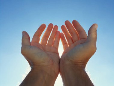 Mavi gökyüzü ile güneşi tutan erkek eller.