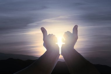 Elleri açık Hristiyan bir adam, haç şeklinde güneş ışığı ve dramatik bir gökyüzü..