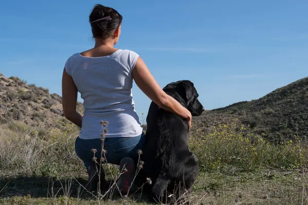 Labrador dog with woman sitting on ground and resting while walking in nature.