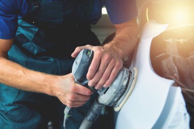 Öğütücü ellerinde. Adam araba boyacısında cila keskinleştiriyor..