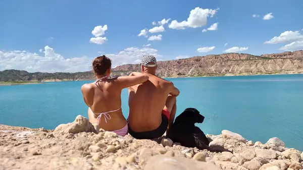 Couple with labrador in nature sitting by the water in summer