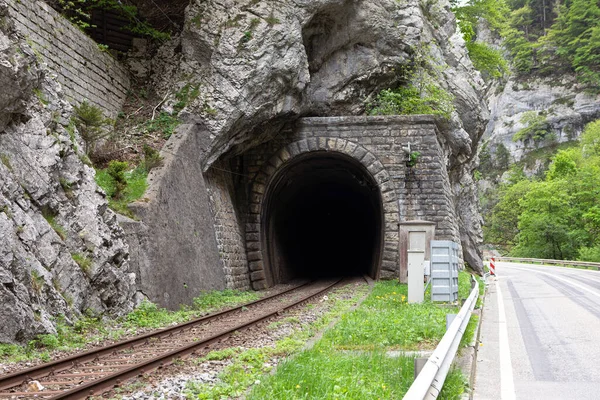 Old train tunnel with railway in a mountain. Dark hollow at tunnel entrance. Swiss railway infrastructure built in the mountains, tunnel enter.