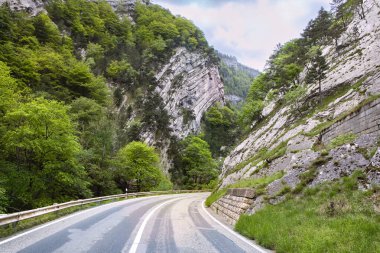 Baharda kayalık dağlarda yol. Güzel dağ kıvrımlı yol, yeşil yapraklı ağaçlar ve bulutlu gökyüzü. İsviçre 'nin Jura Dağları' nda geziyorum..