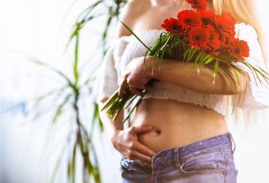 Hamileliğin ilk ayında bir kadının yakın çekimi. Bulanık kız ve odak noktasında çiçekler.