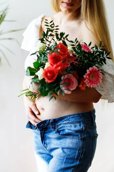 Second month of pregnancy. Close-up of beautiful pregnant girl with flowers. A series of photos of a pregnant girl. Pregnancy, parenthood and expectation concept