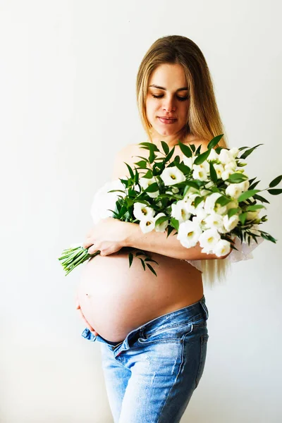 Seventh month of pregnancy. Beautiful pregnant woman with flowers. A series of photos of a pregnant girl. Concept of pregnancy, motherhood, mothers day