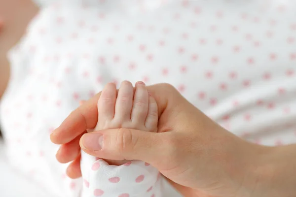 Close up mother holding tiny hand of little newborn baby boy girl, helping hands, bonding different generations. Happy motherhood concept