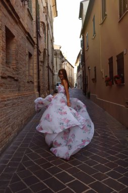 Una giovane ragazza bruna dai capelli fluenti in un abito chic con un grande strascico e una stampa floreale per le strade Italia al tramonto. Yüksek kalite fotoğraf